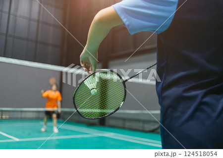 Badminton indoor sport player serving badminton shuttlecock with racket in front of net in game Badminton indoor sport player serving badminton shuttlecock with racket in front of net in game 124518054