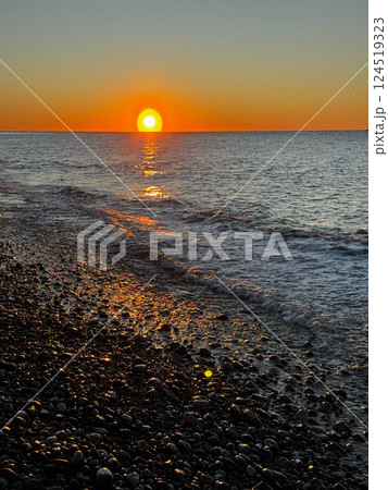 Sunset over pebble beach with shimmering water reflections Sunset over pebble beach with shimmering water reflections 124519323