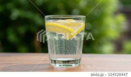 Glass of lemon water with condensation in sunlight and green plant background Glass of lemon water with condensation in sunlight and green plant background 124520447