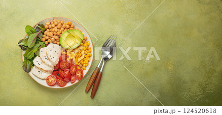 Healthy bowl with chicken breast, chickpeas, avocado, corn and tomatoes on green vibrant background top view. Diet and healthy food concept 124520618