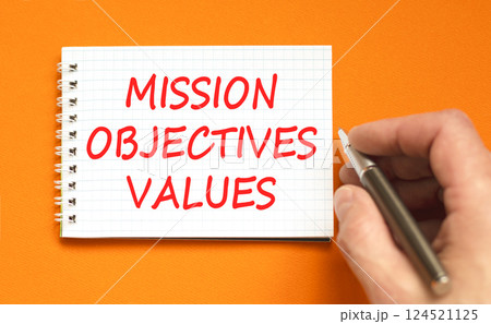 Mission objectives values symbol. Concept words Mission Objectives Values on beautiful white note. Beautiful orange background. Businessman hand. Business mission objectives values concept. Copy space Mission objectives values symbol. Concept words Mission Objectives Values on beautiful white note. Beautiful orange background. Businessman hand. Business mission objectives values concept. Copy space 124521125