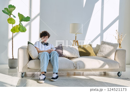 Young guy 20 years old sitting at home on the couch using smartphone 124521173