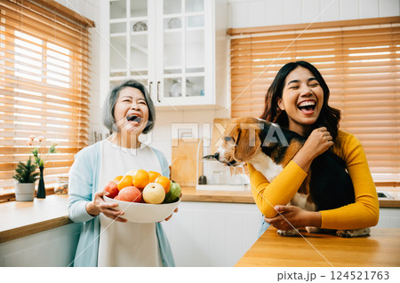 A happy Asian grandmother, her daughter, and young woman share a playful kitchen scene with their Beagle dog, highlighting the fun, happiness, and family bonding over pet care. 124521763