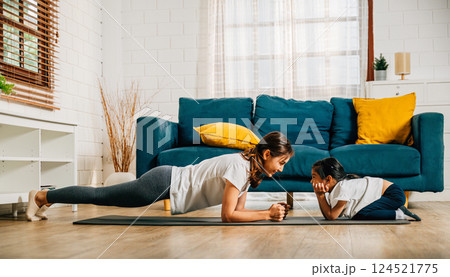 In a cozy atmosphere a mother and her charming daughter practice family yoga stretching and balancing together. Their smiles showcase a happy and harmonious family moment. In a cozy atmosphere a mother and her charming daughter practice family yoga stretching and balancing together. Their smiles showcase a happy and harmonious family moment. 124521775