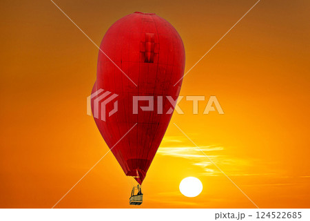Red heart-shaped hot air balloon flying under orange sunset sky Red heart-shaped hot air balloon flying under orange sunset sky 124522685