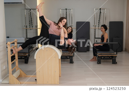 Three women doing Pilates on a reformer and a Pilates barrel. Three women doing Pilates on a reformer and a Pilates barrel. 124523250