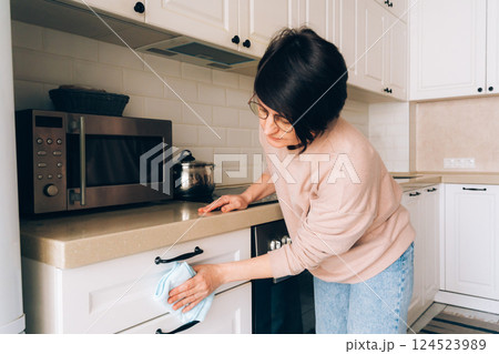 Mature female cleaning kitchen counter in cozy home setting 124523989
