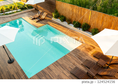 Modern turquoise swimming pool with wooden deck, lounge chairs, and umbrellas in a stylish backyard Modern turquoise swimming pool with wooden deck, lounge chairs, and umbrellas in a stylish backyard 124524156