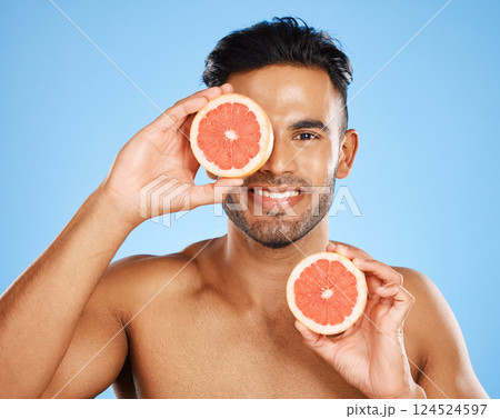 Beauty, grapefruit and skincare with a man model in studio on a blue background to promote natural treatment. Food, wellness and portrait with a handsome young male holding a fruit slice to his face Beauty, grapefruit and skincare with a man model in studio on a blue background to promote natural treatment. Food, wellness and portrait with a handsome young male holding a fruit slice to his face 124524597
