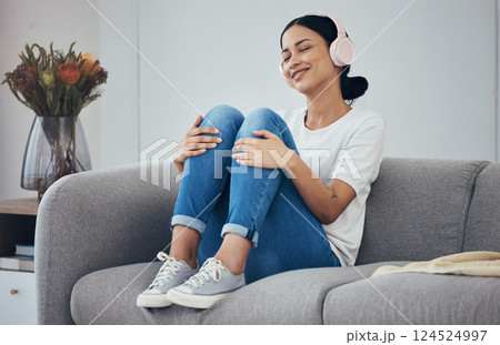 Relax, headphones and woman on sofa in home living room streaming music, podcast or radio. Happy, smile and carefree female from Canada enjoying listening to audio, playlist or favorite song in house 124524997