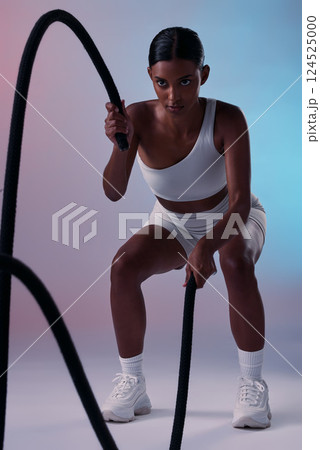 Rope, cardio and woman training for health, fitness and wellness against a colourful studio background. Strong, focus and Indian athlete with battle ropes for exercise, motivation and workout Rope, cardio and woman training for health, fitness and wellness against a colourful studio background. Strong, focus and Indian athlete with battle ropes for exercise, motivation and workout 124525000