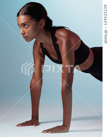 Fitness, exercise and focus with a sports woman in studio on a blue background doing pushups for strong muscles. Training, health and workout with a young female athlete exercising for wellness Fitness, exercise and focus with a sports woman in studio on a blue background doing pushups for strong muscles. Training, health and workout with a young female athlete exercising for wellness 124525139