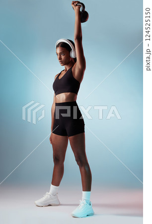 Health, exercise and woman in headphones with kettlebell on a blue studio background. Fitness, sports and female from India streaming music, radio or podcast while training with exercising weight. 124525150
