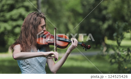 A young girl plays the violin in a city park. Video in motion. 124525426