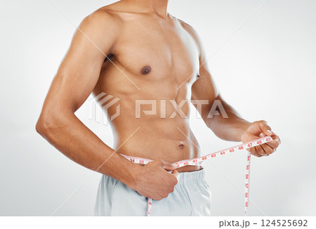 Man, measuring tape with weightloss and diet, body wellness and healthy lifestyle, weight check with bare abdomen. Fitness, health and muscle, shirtless and abs with fat or slim in studio background. 124525692