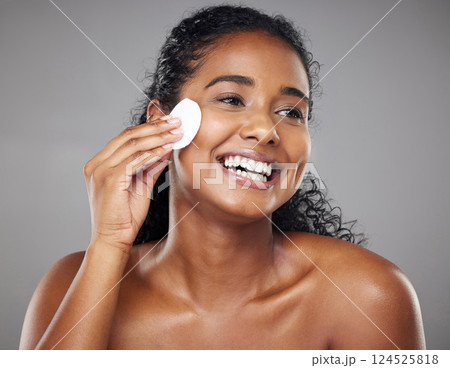 Skincare, cotton pad and woman cleaning face with a smile against a grey studio background. Clean, wellness and African girl model thinking of facial makeup, cosmetic cleansing and care for skin 124525818