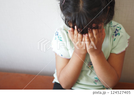 Child covering face with hands while sitting on a bench indoors Child covering face with hands while sitting on a bench indoors 124527405