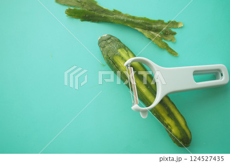 Peeling a cucumber on a turquoise cutting board in a kitchen 124527435