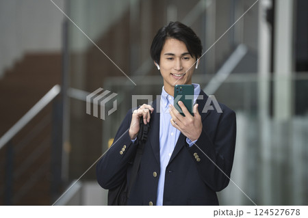 スマートフォンの画面をみるイヤホンをした若いビジネスマン スマートフォンの画面をみるイヤホンをした若いビジネスマン 124527678