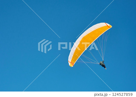 Paraglider flying under clear blue sky Paraglider flying under clear blue sky 124527859
