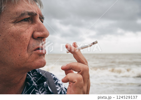 portrait of a sad adult elderly Caucasian man in stress smoking cigarette alone outdoors in nature portrait of a sad adult elderly Caucasian man in stress smoking cigarette alone outdoors in nature 124529137