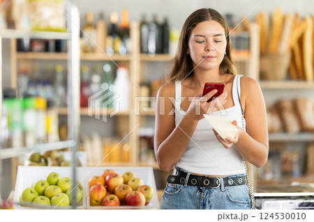 Female shopper scans QR code on cheese label using smartphone. Checking products in supermarket Female shopper scans QR code on cheese label using smartphone. Checking products in supermarket 124530010