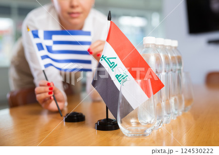 Employee of delegation prepares negotiating table - sets up flag of Greece and Iraq 124530222