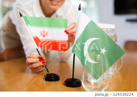 Young woman putting flags of Iran and Pakistan on table in office 124530224