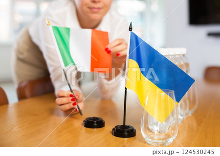 Flags of Ukraine and Italy in female hands preparing negotiating table 124530245