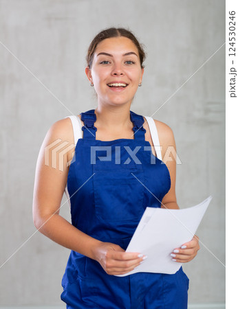 Happy female worker in work clothes standing holding papers Happy female worker in work clothes standing holding papers 124530246