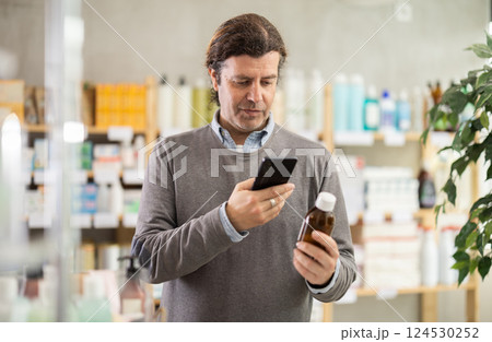 Man in pharmacy scans QR code on expectorant syrup bottle product 124530252