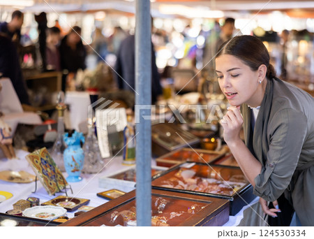 Portrait of smiling young woman choosing vintage goods at flea market Portrait of smiling young woman choosing vintage goods at flea market 124530334