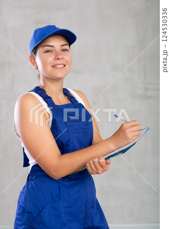 Happy female worker in work clothes making notes in file with papers 124530336