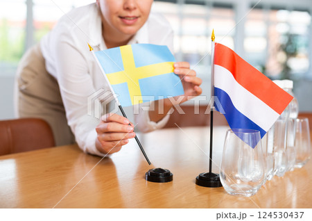 Young woman putting flags of Sweden and Netherlands on table in office Young woman putting flags of Sweden and Netherlands on table in office 124530437