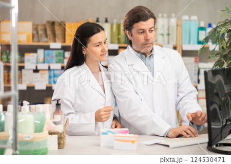 Male and female pharmacists looking for pills and ointment on computer 124530471