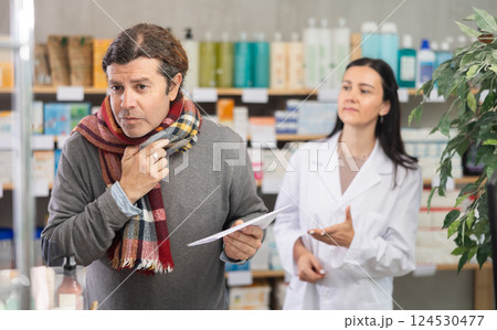 man with a scarf tied around his throat stands in a pharmacy against the background of pharmacist 124530477