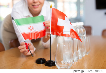 Young woman putting flags of Iran and Switzerland on table in office Young woman putting flags of Iran and Switzerland on table in office 124530498