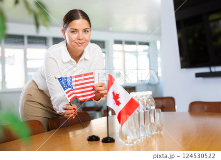 Young woman puts flags of USA and Canada on table in office 124530522