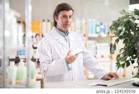 Friendly male pharmacist standing at drugstore with medical product in hands 124530556