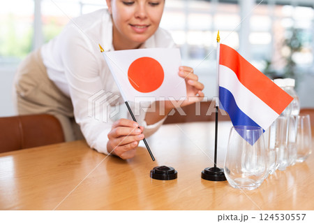 Young woman putting Japan and Netherlands flags on table in office 124530557