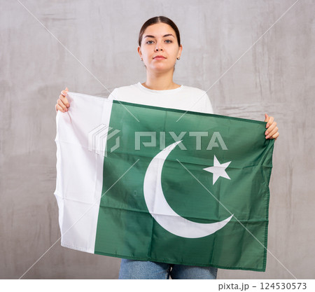Serious young female with flag of Pakistan against background of gray wall 124530573