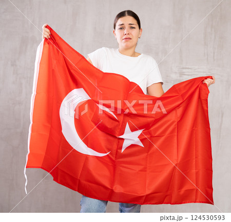 Sad young woman holding Turkey flag against unicoloured background Sad young woman holding Turkey flag against unicoloured background 124530593