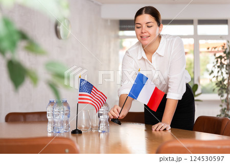 Female secretary places flags of the USA and France on the table before negotiations of top political figures 124530597