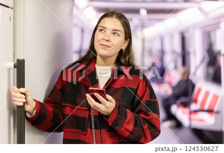 Girl is standing with phone in subway car, getting to work Girl is standing with phone in subway car, getting to work 124530627