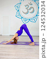 Woman practicing downward-facing dog yoga pose on a purple mat 124532034