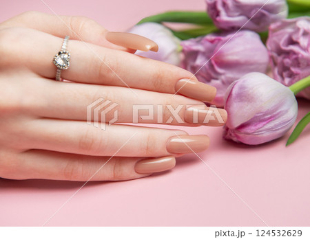 Woman showing nude manicure and engagement ring near tulips on pink background Woman showing nude manicure and engagement ring near tulips on pink background 124532629