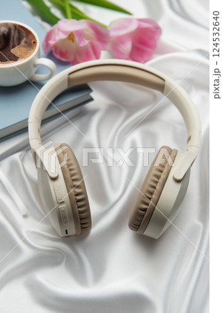 Wireless headphones, coffee, book, and pink tulips resting on white silk Wireless headphones, coffee, book, and pink tulips resting on white silk 124532640