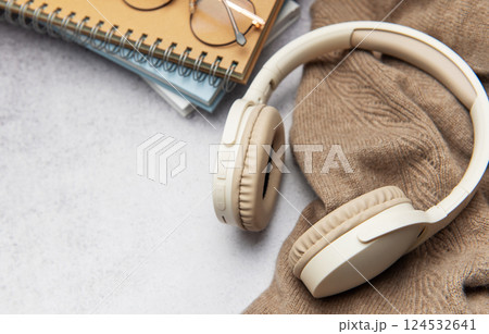 Wireless headphones, eyeglasses and notebooks resting on cozy sweater 124532641