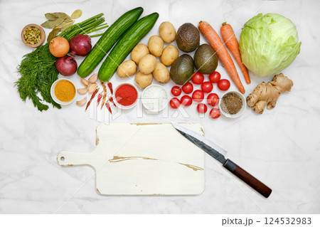 Variety of fresh vegetables and dry spice on a marble table alongside white chopping board and a knife 124532983