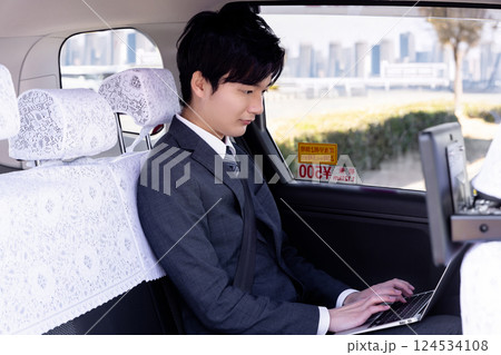 タクシーの後部座席でノートパソコンを使うビジネスマン タクシーの後部座席でノートパソコンを使うビジネスマン 124534108
